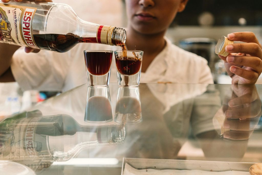 한 사람이 병과 뚜껑을 들고 반사 표면의 두 개의 작은 안경에 어두운 액체를 붓습니다.