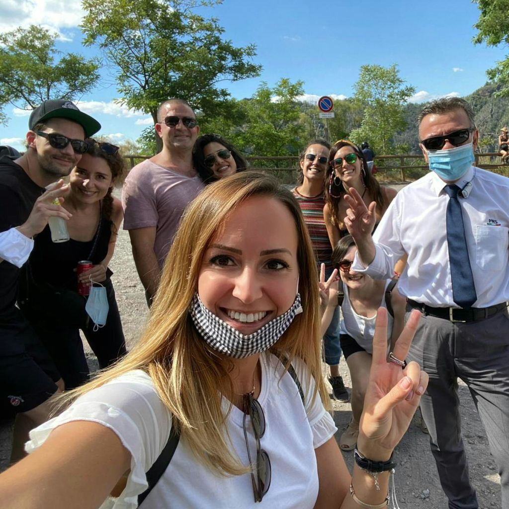 야외에서 웃고 있는 사람들 중 한 명은 마스크를 쓰고 다른 한 명은 마스크를 내려 화창한 날에 사진을 찍기 위해 포즈를 취하고 있습니다.