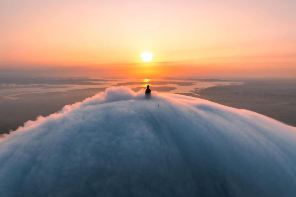 한 사람이 구름으로 둘러싸인 봉우리에 서서 고요하고 광활한 풍경을 바라보며 먼 석양을 바라보고 있습니다.