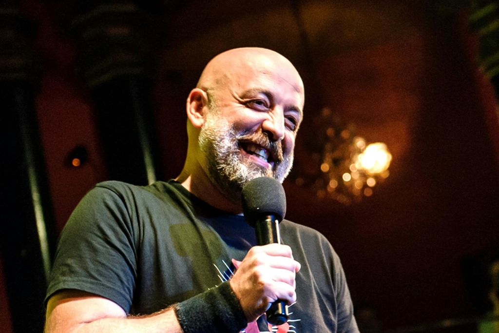 무대에서 따뜻한 조명과 흐릿한 배경으로 미소를 짓고 있는 마이크를 들고 있는 사람.