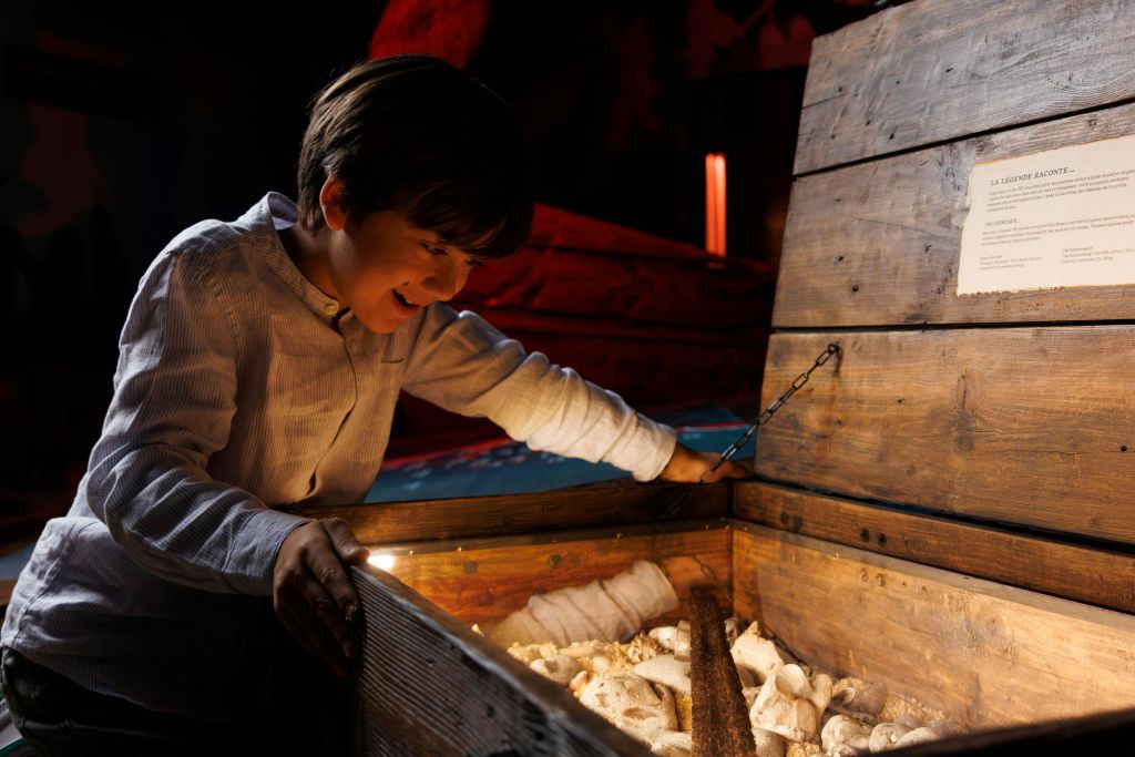 어린 소년이 희미한 조명으로 따뜻하게 비춰진 다양한 물건이 가득한 열린 나무 상자를 신나게 들여다보고 있습니다.