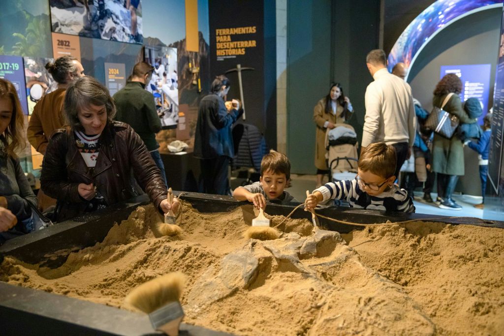 박물관 전시관의 샌드박스에서 브러시를 사용하여 물건을 발견하는 어린이와 성인.