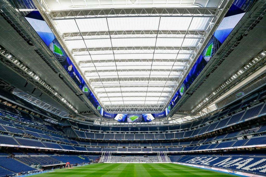 개폐식 지붕, 대형 디지털 스크린, 중앙에 녹색 축구장이 있는 현대적인 경기장입니다.