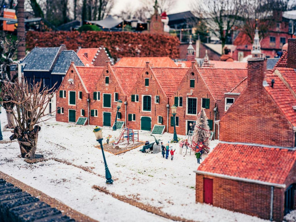 눈 덮인 땅, 벽돌 주택, 놀이터, 사람 형상이 있는 모형 마을. 배경은 나무와 울타리를 보여줍니다.