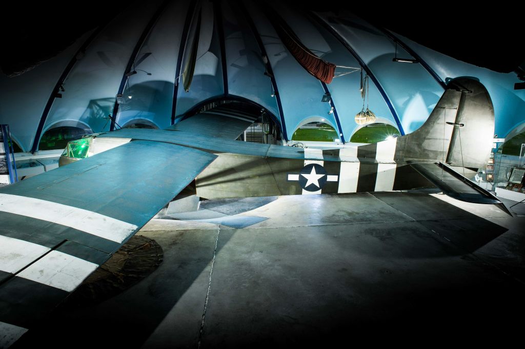 항공 테마의 인테리어를 강조하는 부드러운 조명이 있는 파란색 아치형 구조 아래 전시된 빈티지 항공기 꼬리.