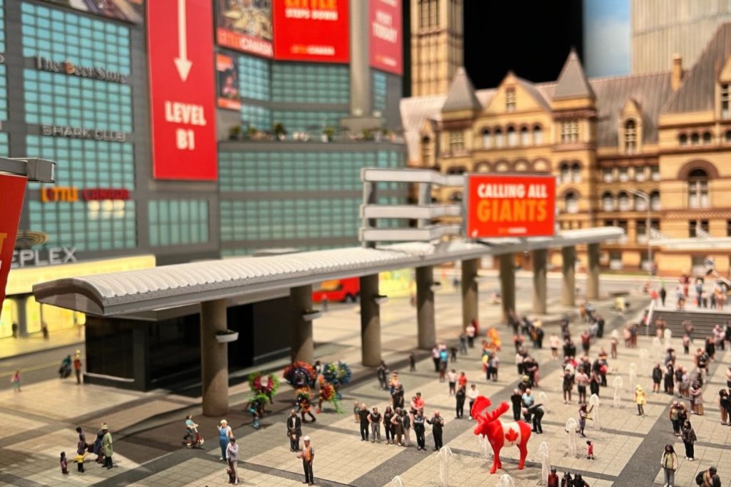 리틀 토론토의 산코파 광장에 서 있는 미니어처 무스 모리스. 미니어처 피규어들이 물 주변으로 모여듭니다.