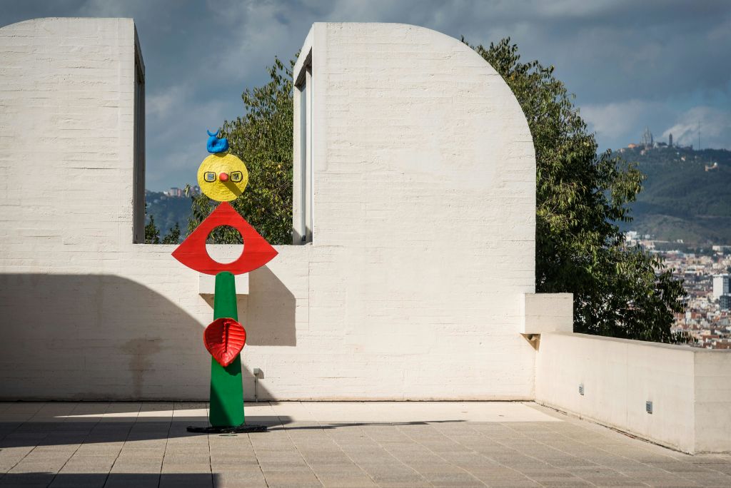 나무와 흐린 하늘을 배경으로 하얀 기하학적 벽을 배경으로 한 다채로운 추상 조형물.