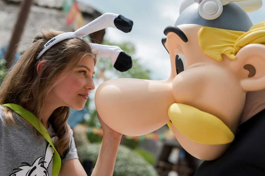 참신한 토끼 귀를 착용한 여성이 만화 같은 풍선 물체를 야외에서 바라보고 있습니다.