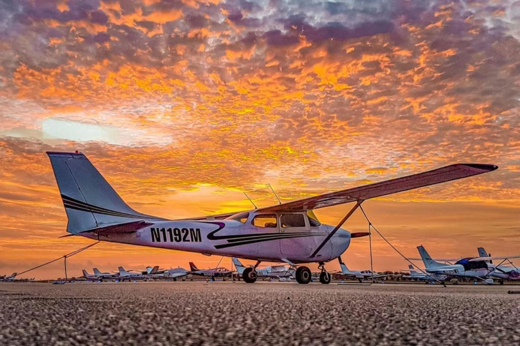 활기찬 주황색, 노란색, 보라색 노을을 배경으로 활주로에 주차된 작은 비행기.