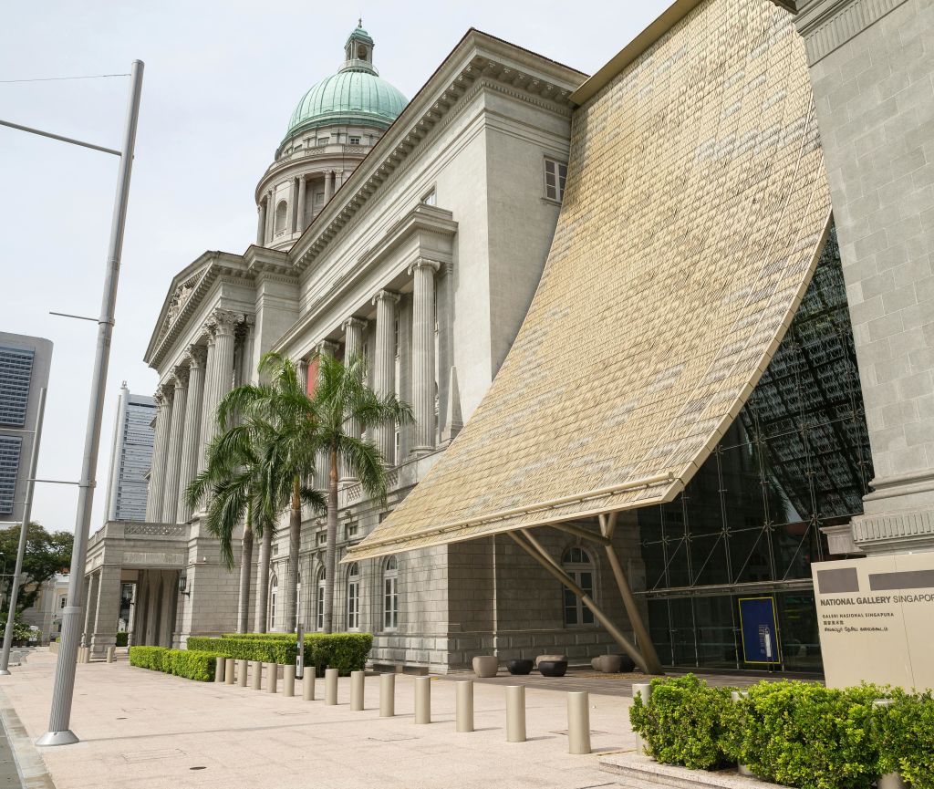 기둥과 녹색 돔이 있는 역사적인 건물에는 커다란 황금색 캐노피가 있는 현대적인 유리 연장선이 있습니다.