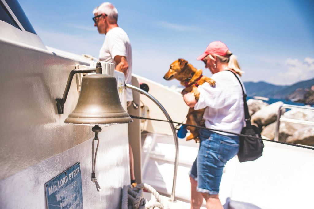 한 명은 개를 안고 배를 타고 있고, 한 명은 맑고 푸른 하늘 아래 전경에 보이는 종을 들고 있습니다.