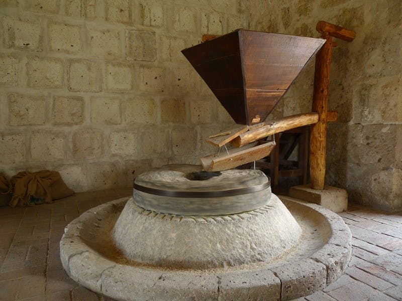 돌담과 나무 기둥이 있는 소박한 방에는 나무 호퍼가 달린 고풍스러운 돌방앗간이 서 있습니다.