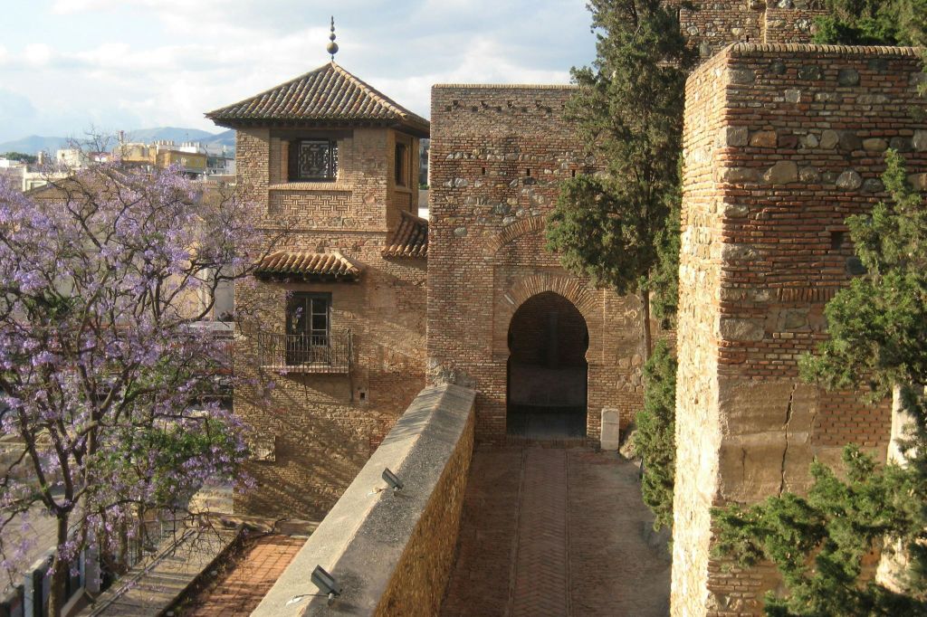 아치형 출입구, 타일 지붕, 오른쪽에 나무가 있는 유서 깊은 석조 건물. 경로는 구조물을 향해 이어집니다.