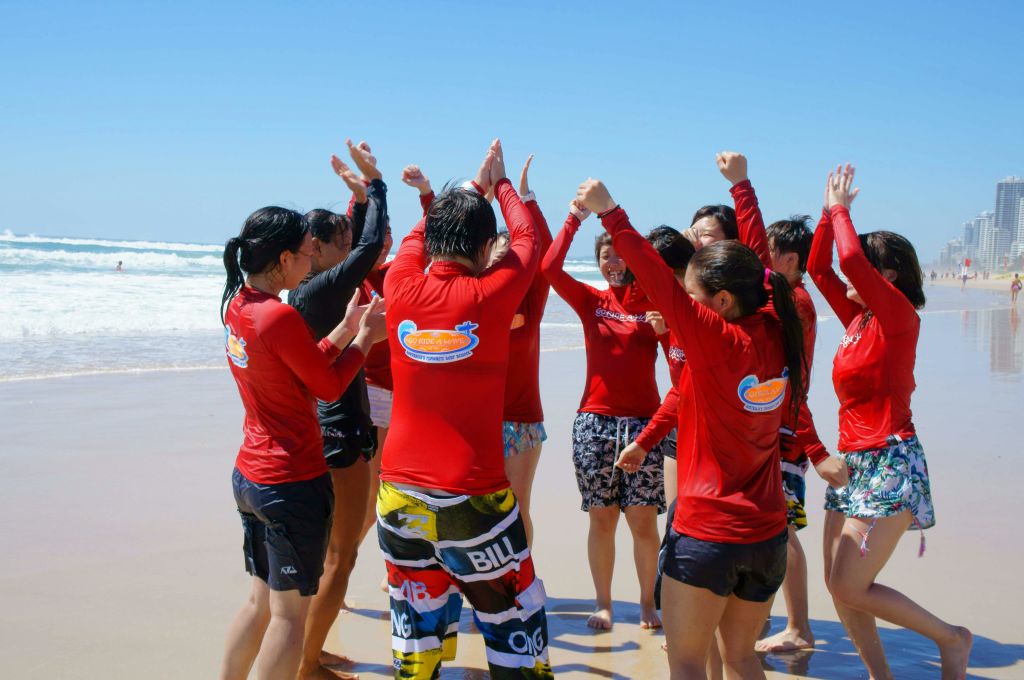 빨간 셔츠를 입고 해변에서 수영복을 입은 한 무리의 사람들이 맑고 푸른 하늘 아래에서 신나게 손을 들고 있습니다.