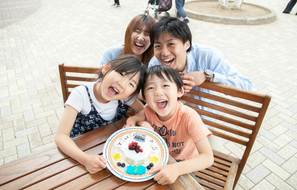 꾸며진 음식 접시가 놓인 테이블에서 네 명이 미소를 짓고 있습니다. 좌석이 있는 야외 공간으로 보입니다.