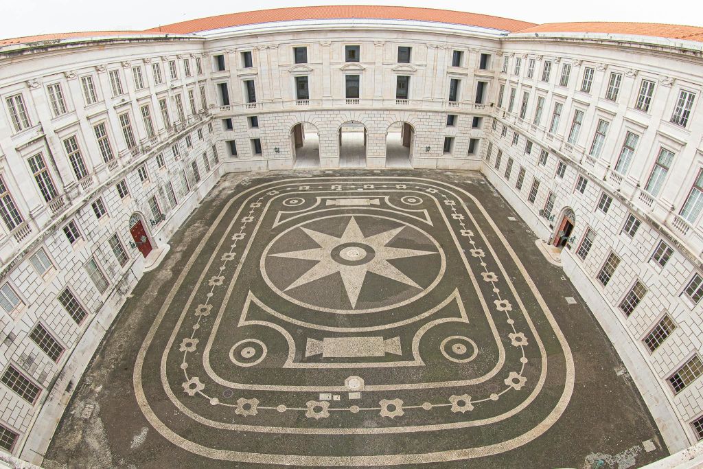 기하학적 돌 무늬가 있는 넓은 안뜰은 아치형 출입구와 창문이 있는 3층 건물로 둘러싸여 있습니다.