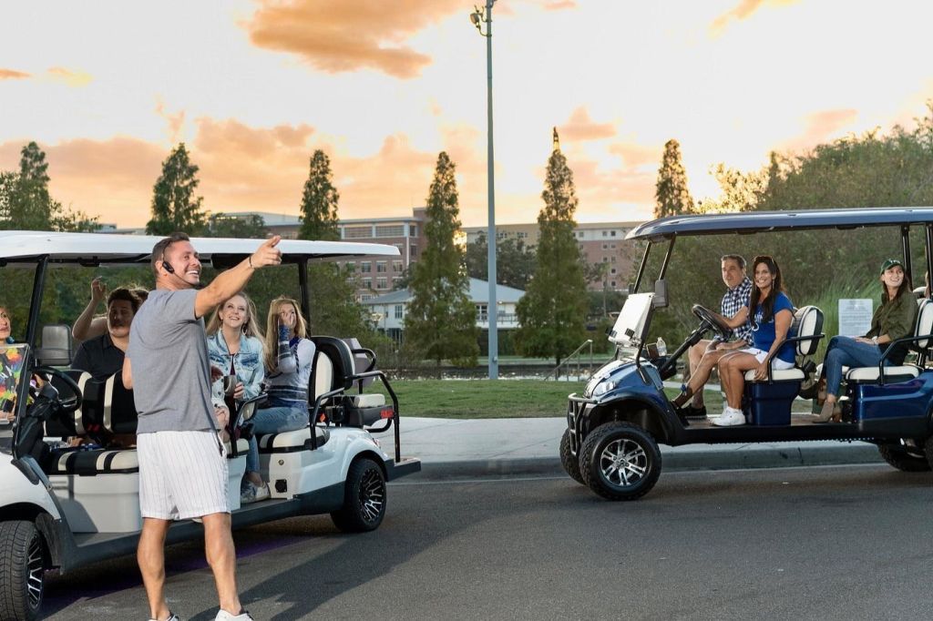 해가 질 무렵 건물과 나무를 배경으로 한 남성이 서서 골프 카트를 타고 있습니다.