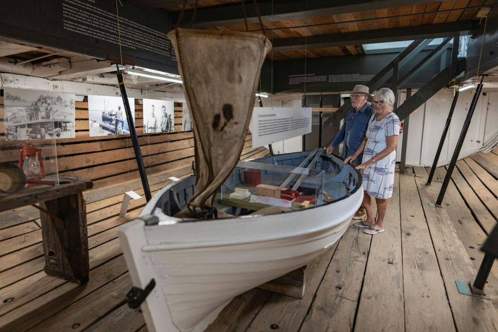 한 노인이 정보 디스플레이가 있는 나무 바닥 박물관 내부의 작은 보트 전시물을 살펴보고 있습니다.