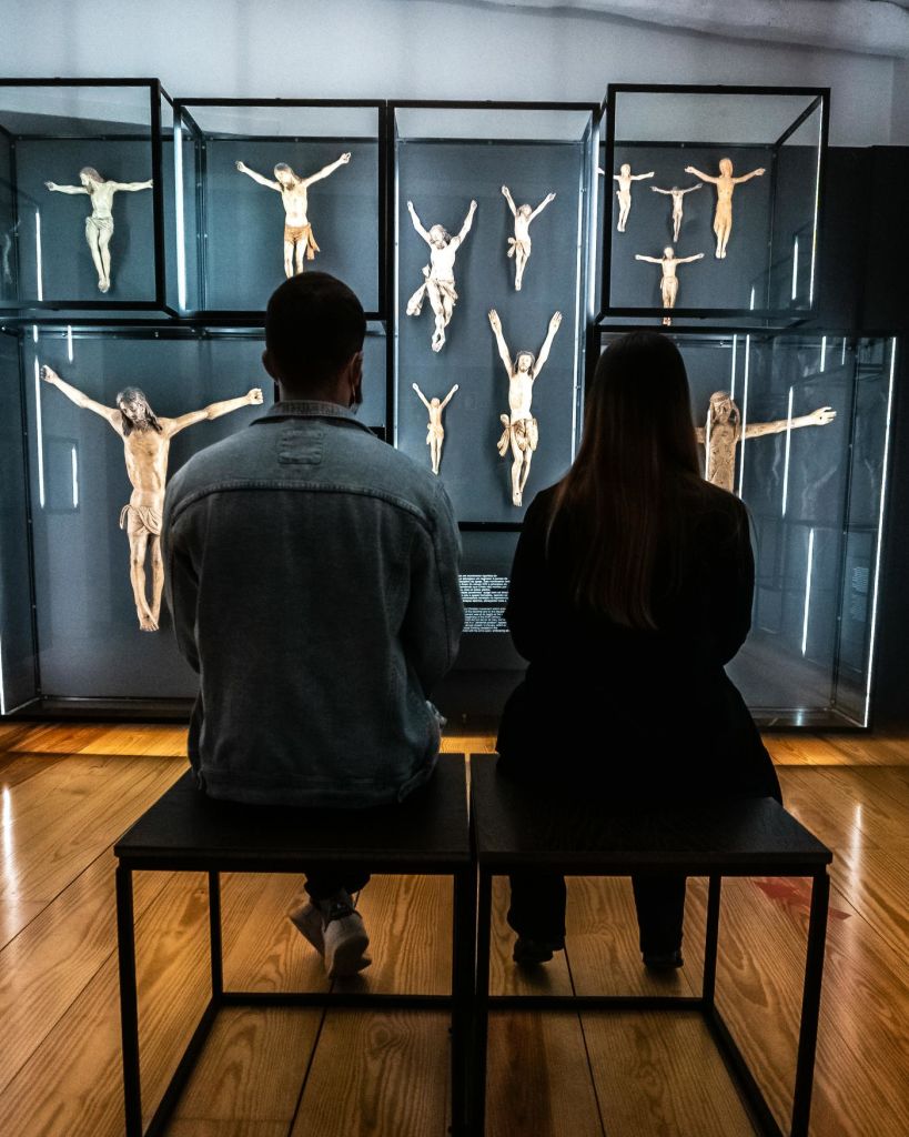 의자에 앉은 두 사람이 박물관에서 십자가에 못 박힌 조각품을 전시하고 있습니다.