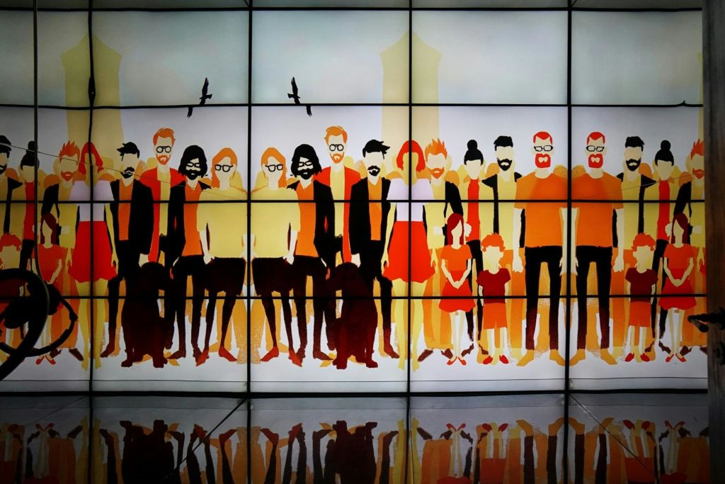 새가 있는 도시 풍경을 배경으로 다채로운 의상을 입은 다양하고 양식화된 사람들의 추상적인 벽화. 아래는 반사 바닥입니다.