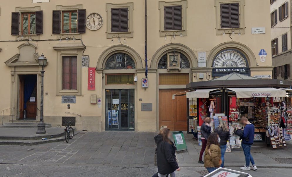 아치형 출입구와 박물관 표지판이 있는 건물의 거리 전망, 산책하는 사람들, 오른쪽에 신문 가판대.