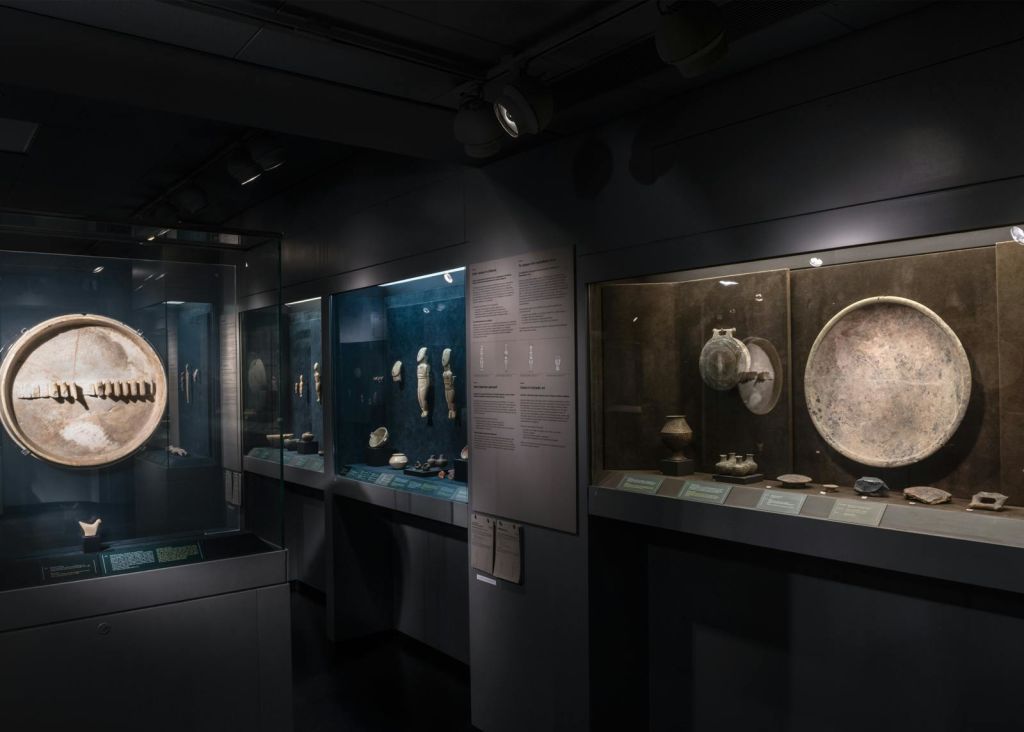 고대 유물과 도자기를 유리 케이스에 담아 서술된 명판으로 전시하는 희미한 조명의 박물관입니다.