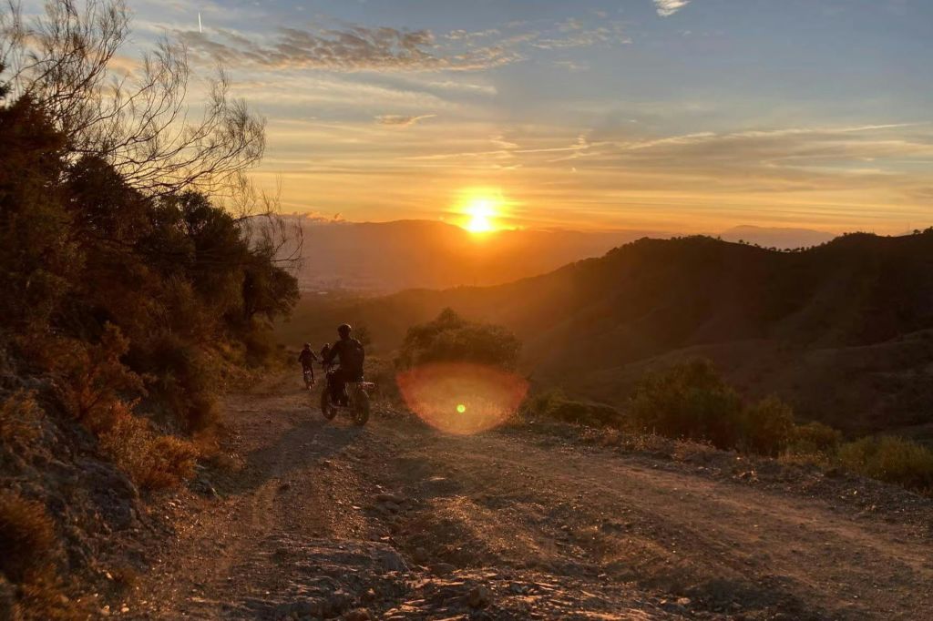 일몰에 험준한 산길에서 흙 자전거를 타는 두 사람은 구불구불한 언덕의 경치와 화려한 하늘을 감상할 수 있습니다.