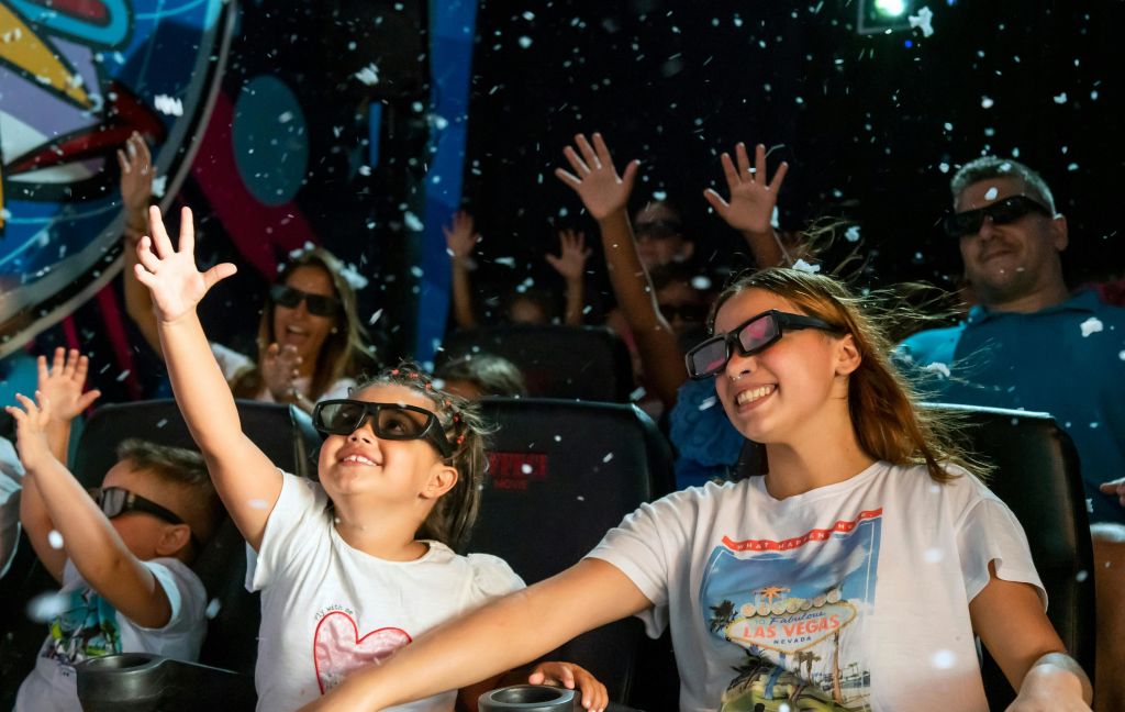 3D 안경을 쓴 어린이와 성인은 극장에 앉아 미소를 지으며 손을 들고, 주변에 콘페티나 눈이 내립니다.