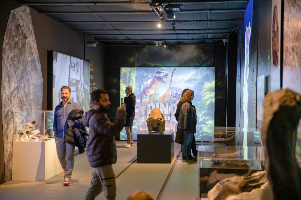 박물관의 공룡 전시관을 거닐고 있는 사람들은 공룡의 대형 일러스트를 볼 수 있습니다.