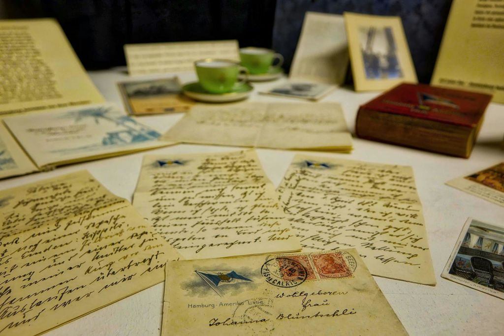 초록색 찻잔, 액자 사진, 빨간색 책으로 둘러싸인 테이블 위에 놓인 빈티지 편지와 엽서.