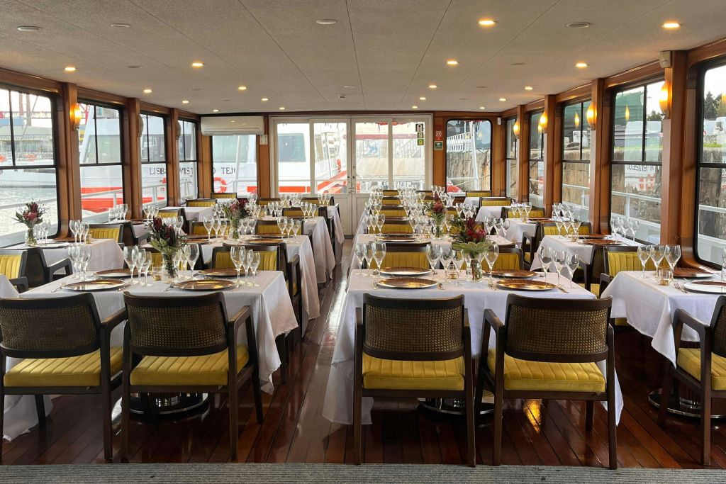 커다란 창문이 있는 보트에 흰색 식탁보, 노란색 의자, 꽃 센터피스가 있는 깔끔한 식사 공간입니다.