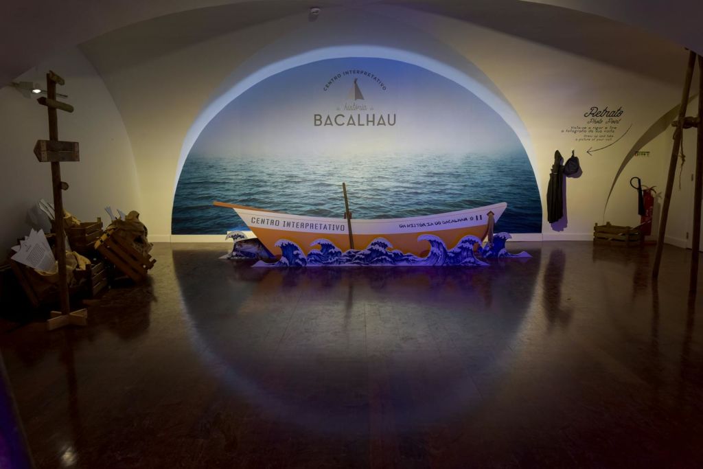 "Centro Interpretativo" 라고 표시된 작은 보트가 "Bacalhau" 라는 글자와 함께 바다 벽화 앞에 있는 파도 디스플레이에 놓여 있습니다.