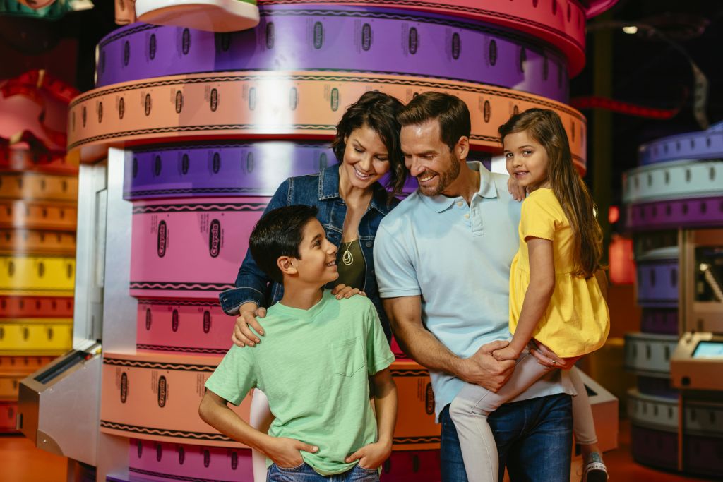 네 명으로 구성된 웃는 가족이 쌓인 원형 사물이나 장식이 있는 화려한 배경 앞에 서 있습니다.