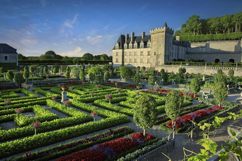 맑고 푸른 하늘 아래 역사적인 석조 성 앞에 화려한 화단과 울타리가 있는 잘 손질된 정원.