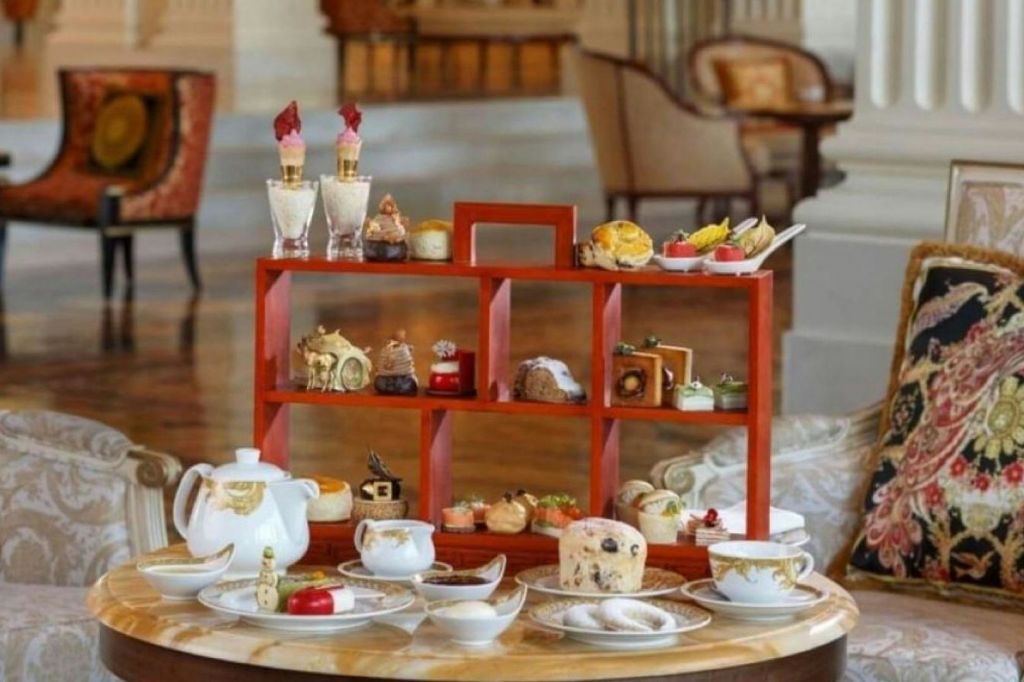 다양한 작은 페이스트리와 디저트를 전시한 나무로 된 계단식 쟁반에 흰색 식탁보 위에 차 세트가 놓여 있습니다.