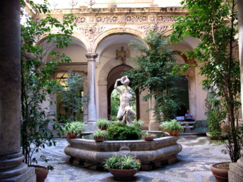 녹지와 기둥, 화려한 디자인의 아치형 벽으로 둘러싸인 중앙 동상 분수가 있는 마당입니다.