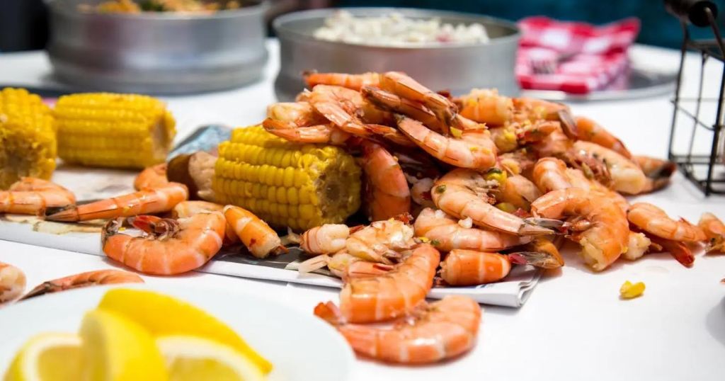 옥수수 속의 조리된 새우와 옥수수는 다른 요리를 배경으로 테이블에 놓여 있습니다.