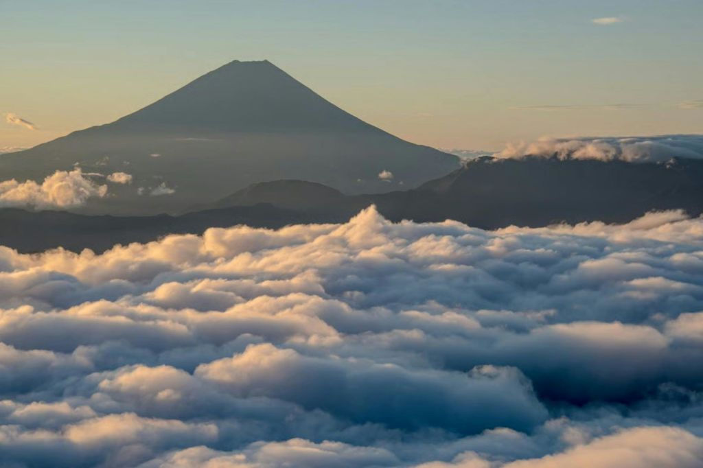 맑은 하늘을 배경으로 일출 시 구름 바다 위로 산봉우리가 솟아 있습니다.