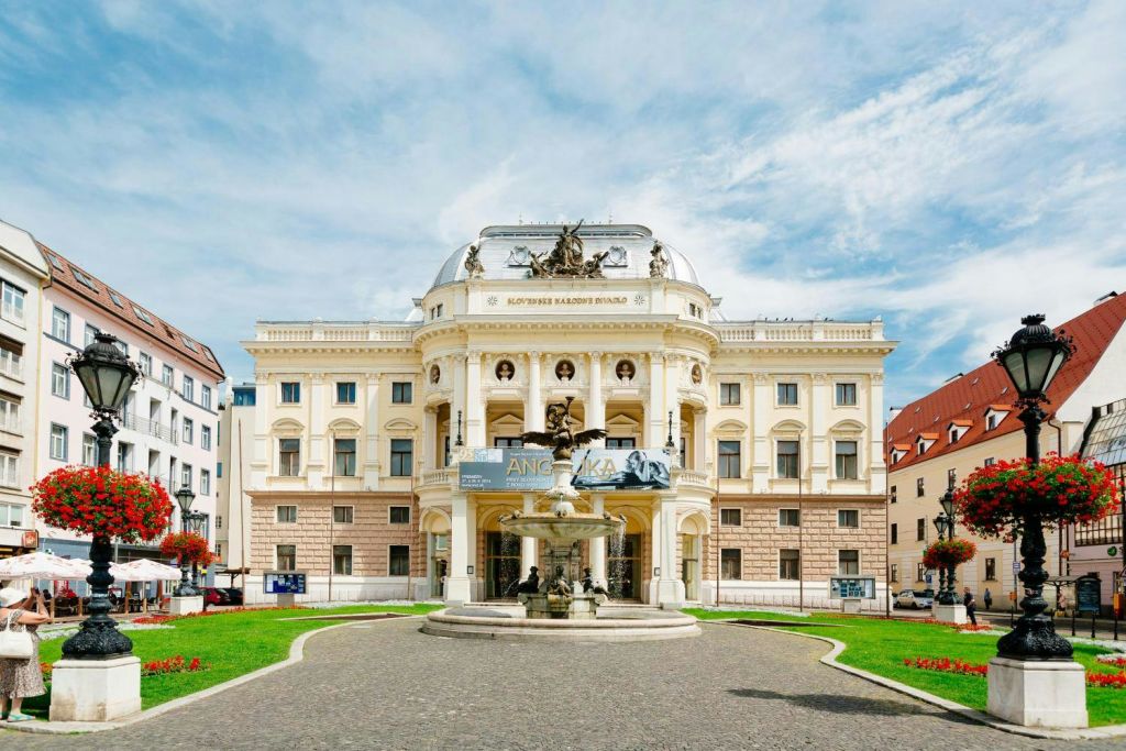 잘 관리된 녹색 잔디밭으로 둘러싸인 대형 배너, 중앙 돔, 앞에 분수가 있는 화려한 극장.