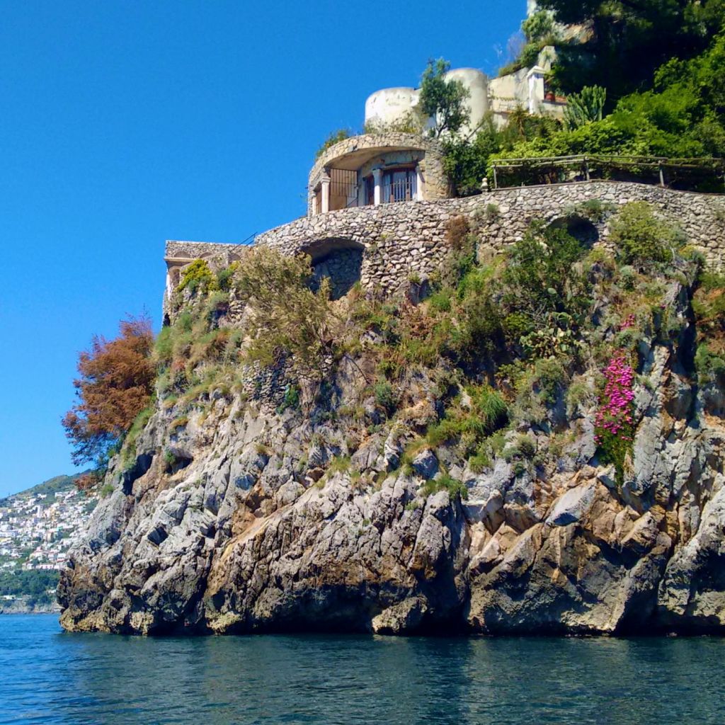 녹음이 우거진 절벽 위에 자리한 석조 건물로, 맑고 밝은 하늘 아래 잔잔하고 푸른 바다가 내려다보입니다.