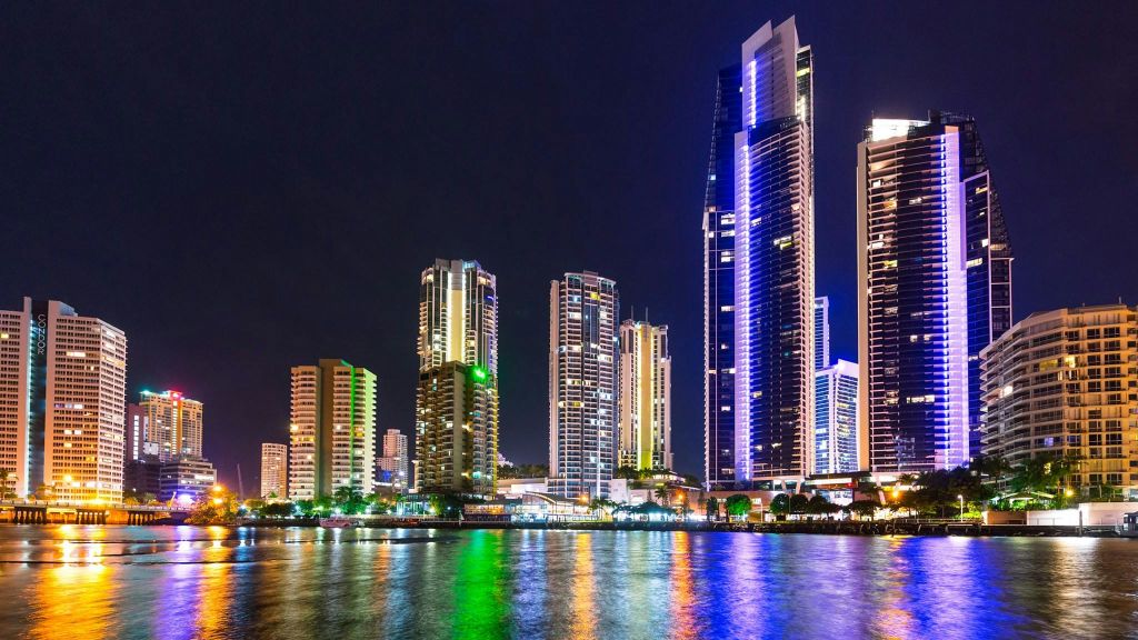 밤에는 도시의 스카이라인 아래 물 위에 활기찬 빛을 반사하는 조명으로 빛나는 고층 건물이 있습니다.