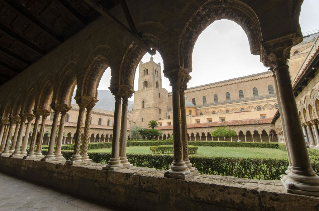 중세의 회랑을 배경으로 아치형 콜로네이드, 중앙 정원, 석탑이 내려다보입니다.