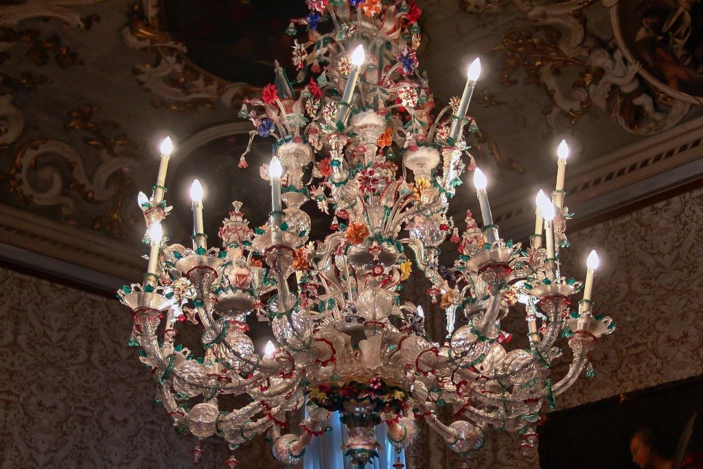 화려한 꽃 장식으로 장식된 촛불이 달린 크고 화려한 크리스탈 샹들리에가 정교하게 장식된 천장에 매달려 있습니다.