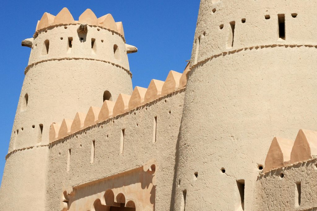 맑고 푸른 하늘 아래 타워와 장식용 크레넬이 있는 어도비 요새의 클로즈업.