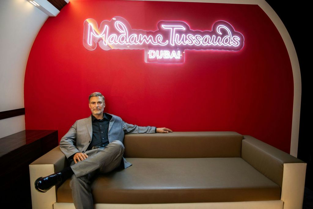 마담 투소 두바이 (Madame Tussauds Dubai) 에서 회색 양복을 입은 남성이 네온사인을 배경으로 앉아 있는 모습.