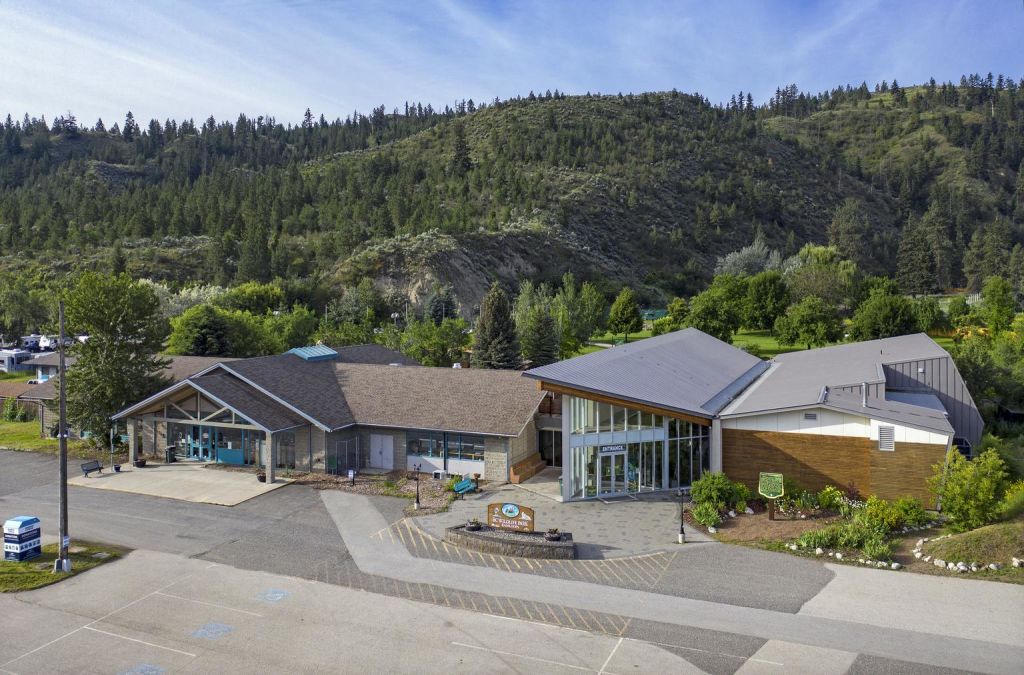 커다란 창문이 있는 현대적인 건물은 맑고 푸른 하늘 아래 녹지로 둘러싸인 숲이 우거진 언덕 아래에 있습니다.