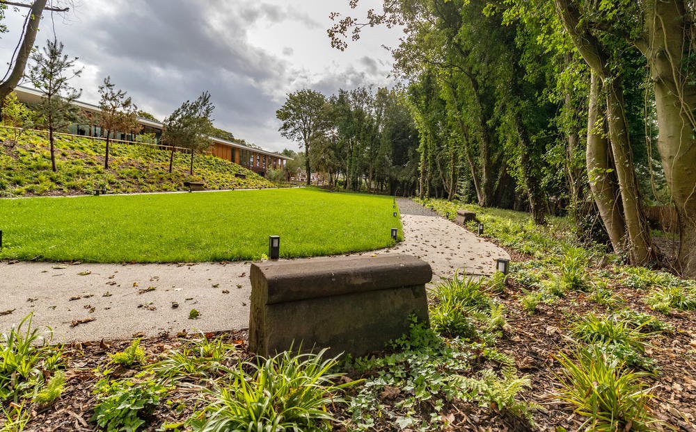 가장자리를 따라 작은 조명과 공원의 벤치가 있는 잔디와 나무로 둘러싸인 곡선형 도로입니다.