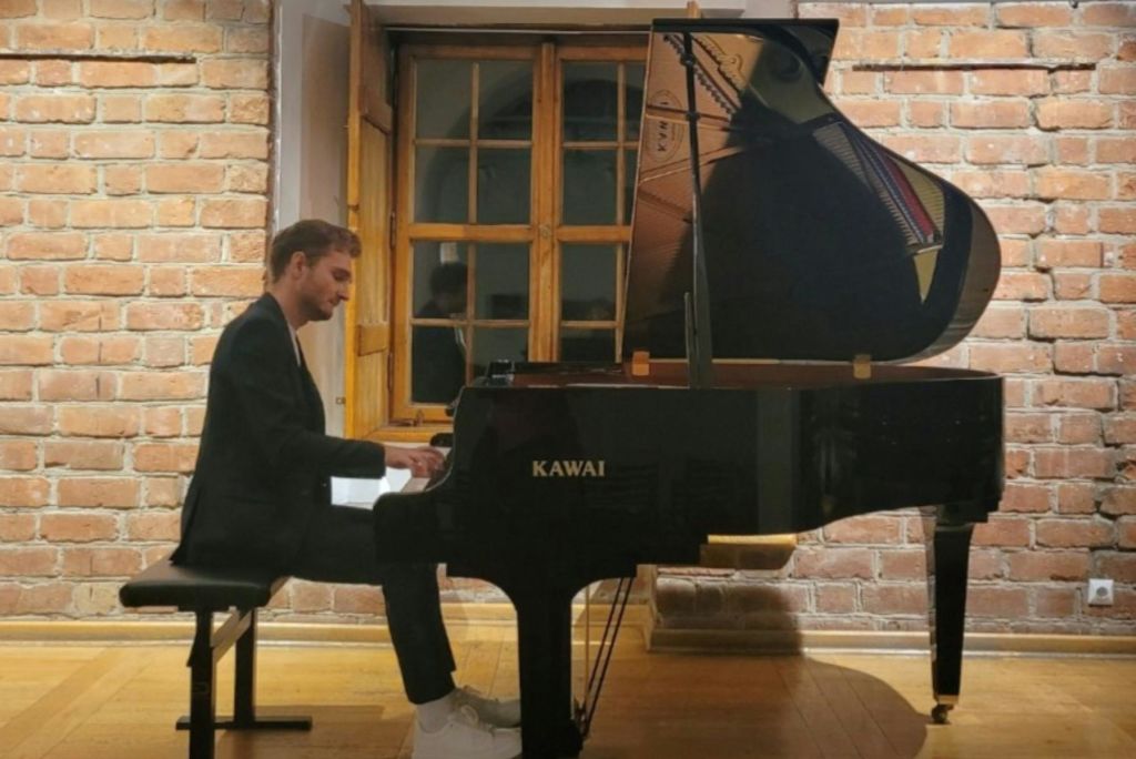 벽돌 벽과 나무 창문이 있는 방에서 그랜드 피아노를 연주하는 사람.