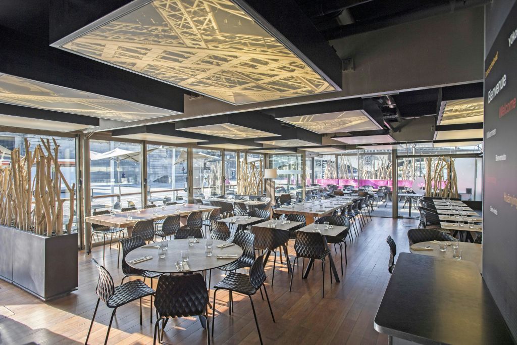 텅 빈 검은색 의자와 원형 테이블, 조명 천장 패널, 커다란 창문으로 야외 전망을 감상할 수 있는 현대적인 레스토랑입니다.