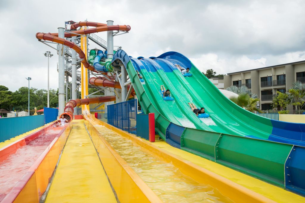 흐린 날 워터파크에서 형형색색의 물 미끄럼틀을 타고 내려오는 사람들.